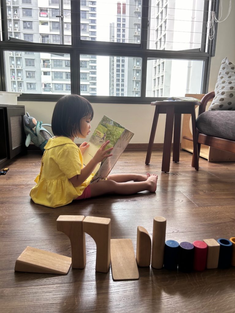 A girl in a yellow dress sits on a living room floor, holding a picture book and reading.